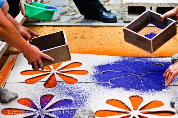 Sifting blue sawdust (aserrín) flowers on to the orange base using a cardboard stencil, Antigua, Guatemala